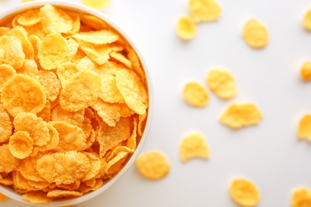 White cup with golden corn flakes, isolated on white background. Hopya crumbled around the cup. View from above. Delicious and healthy breakfastの写真素材