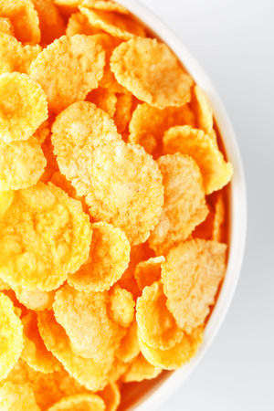 White cup with golden corn flakes, isolated on white background. View from above. Delicious and...