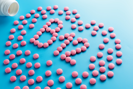 Pink tablets in the form of B12 in the heart on a blue background, spilled from a white can. Food supplement conceptの写真素材