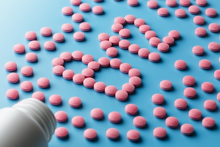 Pink tablets in the form of B12 in the heart on a blue background, spilled from a white can. Food supplement conceptの写真素材