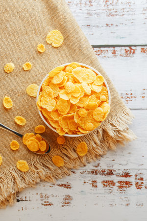 Bowl with golden flakes on a linen, on a light wooden table, next to a spoon. Rustic country style....