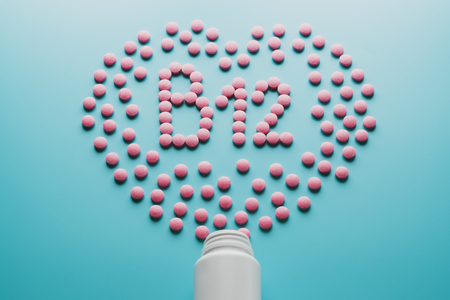 Pink tablets in the form of B12 in the heart on a blue background, spilled from a white can. Food supplement conceptの写真素材