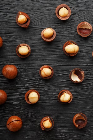 Purified and shell repeats macadamia nuts on black textural stone background. Healthy eating concept. The most expensive nut in the world, growing in Australiaの写真素材