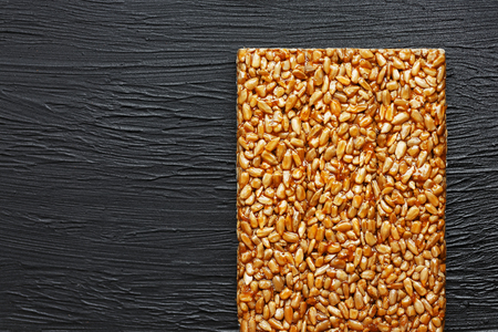 Tile kozinaki from sunflower seeds on a black textural background. Delicious oriental sweets Gozinaki from sunflower seeds, sesame seeds and peanuts, covered with honey with a shiny icing. View from aboveの写真素材