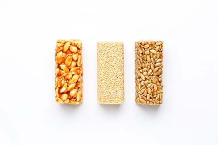 Grain granola bar with peanuts, sesame and seeds in a row on a white background. Top view Three assorted bars, isolateの写真素材