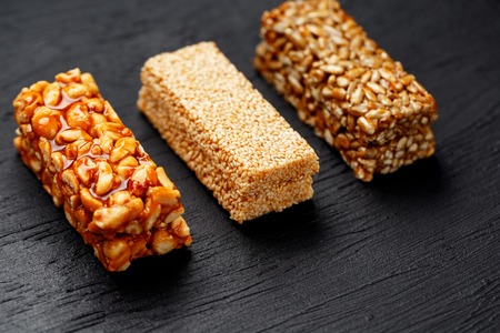 Cereal granola bar with peanuts, sesame and sunflower seeds on a cutting board on a dark stone table. View from above. Three Assorted Barsの写真素材