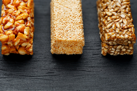 Cereal granola bar with peanuts, sesame and sunflower seeds on a cutting board on a dark stone table. View from above. Three Assorted Barsの写真素材