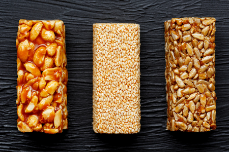 Cereal granola bar with peanuts, sesame and sunflower seeds on a cutting board on a dark stone table. View from above. Three Assorted Barsの写真素材