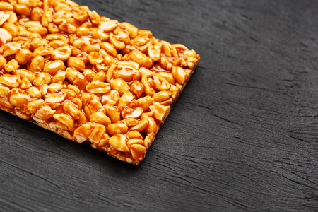 A large golden tile of peanuts, a bar in a sweet molasses on a black texture background. Kozinaki useful and tasty sweets of the East. View from aboveの写真素材