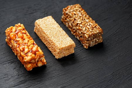 Cereal granola bar with peanuts, sesame and sunflower seeds on a cutting board on a dark stone table. View from above. Granola bar is a creeping and sweet snack. Three Assorted Barsの写真素材