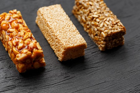 Cereal granola bar with peanuts, sesame and sunflower seeds on a cutting board on a dark stone table. View from above. Granola bar is a creeping and sweet snack. Three Assorted Barsの写真素材