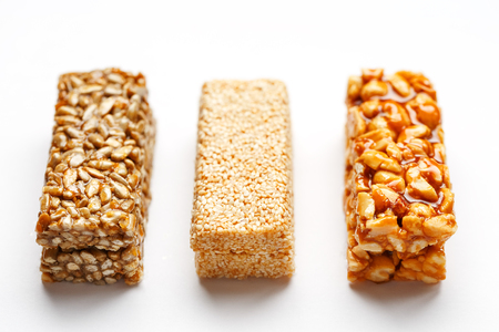 Grain granola bar with peanuts, sesame and seeds in a row on a white background. Top view Kozinaki Three assorted bars, isolateの写真素材