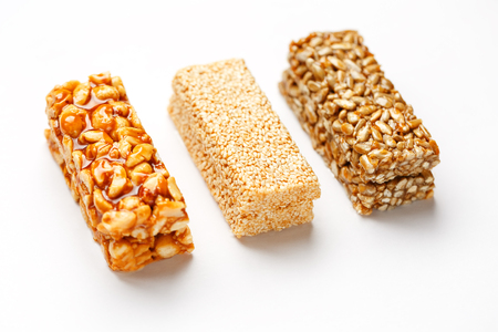 Grain granola bar with peanuts, sesame and seeds in a row on a white background. Top view Kozinaki Three assorted bars, isolateの写真素材