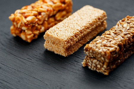 Cereal granola bar with peanuts, sesame and sunflower seeds on a cutting board on a dark stone table. View from above. Granola bar is a creeping and sweet snack. Three Assorted Barsの写真素材