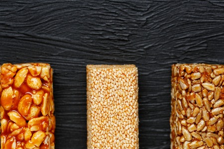 Cereal granola bar with peanuts, sesame and sunflower seeds on a cutting board on a dark stone table. View from above. Granola bar is a creeping and sweet snack. Three Assorted Barsの写真素材