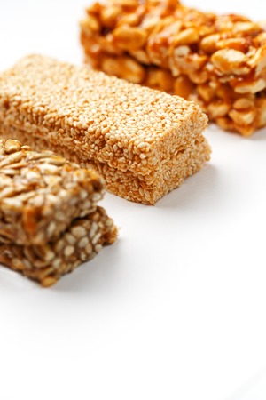 Grain granola bar with peanuts, sesame and seeds in a row on a white background. Top view Kozinaki Three assorted bars, isolateの写真素材