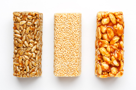 Grain granola bar with peanuts, sesame and seeds in a row on a white background. Top view Kozinaki Three assorted bars, isolateの写真素材