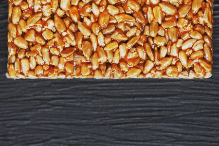 Useful snacks. Fitness diet food. Boletchik from kozinaki sunflower seeds, energy bars. Black textural background Top view. Copy space, low keyの写真素材