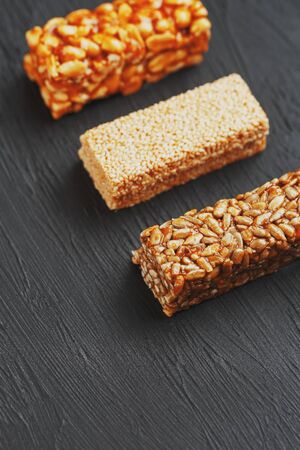 Healthy snacks. Fitness diet food. Grain bar with peanuts, sesame and seeds on a cutting board on a dark table, energy bars. Black background top view. Isolate, Copy Spaceの写真素材