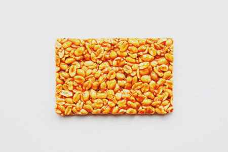 A large tile of roasted peanuts bar in a sweet molasses on a white background. Kozinaki useful and...