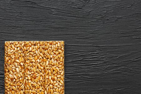 Useful snacks. Fitness diet food. Boletchik from kozinaki sunflower seeds, energy bars. Black textural background Top view. Copy space, low keyの写真素材
