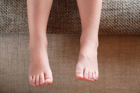 Children's legs close-up hanging from the sofa in the room. Baby toes while baby is sitting on the armchair. Conceptの写真素材