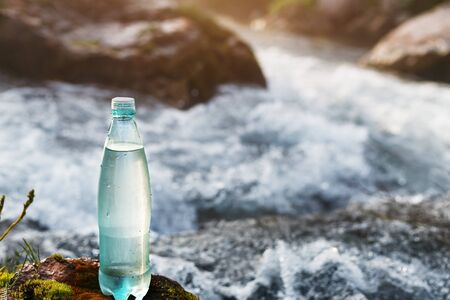 Transparent plastic A bottle of clean water in the grass and moss against the backdrop of a stormy mountain river. The concept of pure natural drinking waterの写真素材