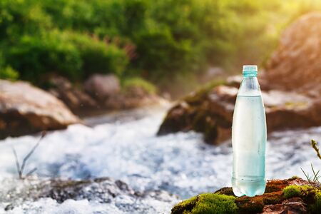 Transparent plastic A bottle of clean water in the grass and moss against the backdrop of a stormy mountain river. The concept of pure natural drinking waterの写真素材