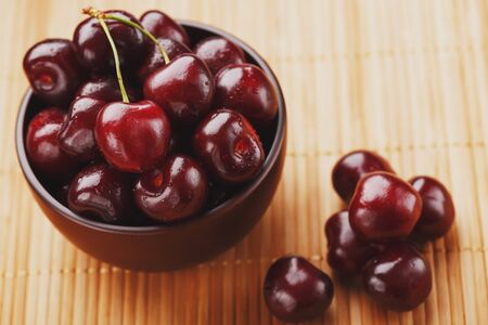 Ripe and juicy cherry berries on a wooden background in a brown cup. Top view, close-up.の写真素材