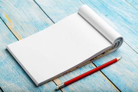 Notepad with red pencil on a blue wooden table background, for education, write goals and deeds. Free white space for writing on a blank sheet of notebook, concept.の写真素材