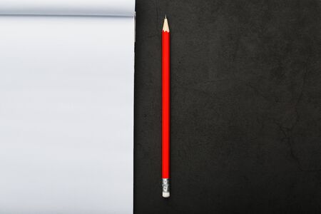 Notepad with a red pencil on a black stone plate background, for education, recording goals and deeds. Free white space for writing on a blank sheet of notebook, concept.の写真素材