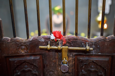 Lock on the ancient door of the Indian temple with a lattice and bolt. Red flower on the lattice.