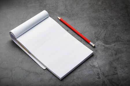 Notepad with a red pencil on a black stone plate background, for education, recording goals and deeds. Free white space for writing on a blank sheet of notebook, concept.の写真素材