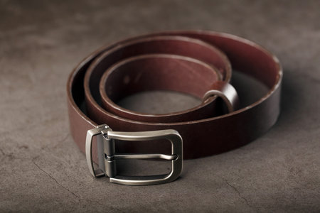 Fashionable men's brown belt made of genuine leather with a light metal buckle on a dark background....