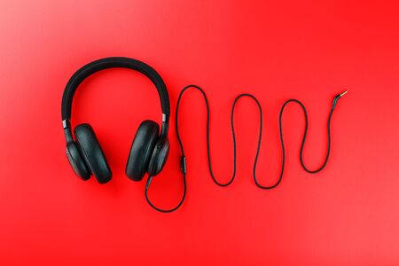 Wireless black headphones on a red background. View from above. In-ear headphones for playing games and listening to music tracks. Modern styleの写真素材
