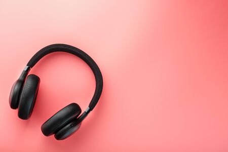 Wireless black headphones on a pink background. View from above. In-ear headphones for playing games and listening to music tracks. Modern styleの写真素材