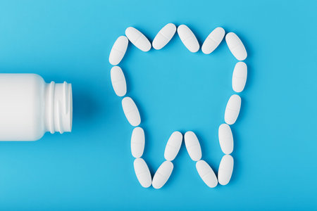 Tooth made of white vitamins with calcium on a blue background. Vitamins spilled out of a...