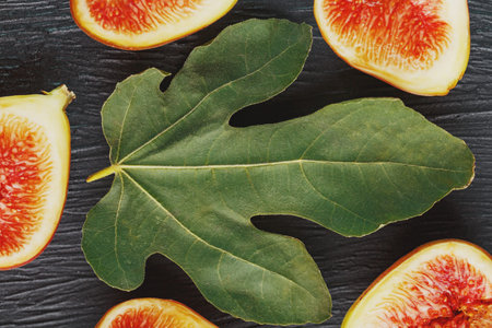 Juicy Figs on a dark background and a large leaf, pulp of fig slices with seeds close-up. The fig...
