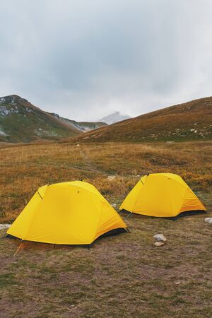 Two yellow tent on a background of a valley with mountains in autumn. Travel and tourism.の写真素材