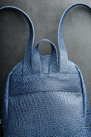 Blue backpack made of genuine leather on a dark background, handmade. Close up and in detail.