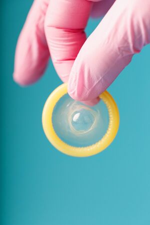 Condom contraception A hand in a pink glove holds a condom on a blue background. Latex for semen and protection against pregnancy. Condom as a contraceptive.の写真素材
