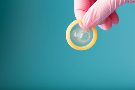 An opened condom in a hand in a pink glove holds on a blue background. Latex for protection against pregnancy.の写真素材