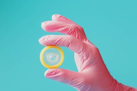 An opened condom in a hand in a pink glove holds on a blue background. Latex for protection against pregnancy. Condom as a contraceptive.の写真素材