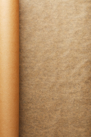 A roll of unfolded brown parchment paper, for baking food in on a dark background, top view. Papyrus