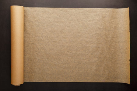 A roll of unfolded brown parchment paper, for baking food in on a dark background, top view. Papyrus