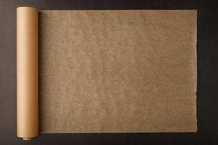 A roll of unfolded brown parchment paper, for baking food in on a dark background, top view. Papyrusの写真素材