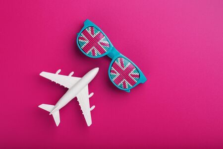 Turquoise sunglasses with United Kingdom flag in lenses on crazy pink background with white airplane. Travelling to England. Freedom and equalityの写真素材