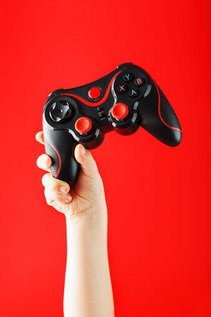 A child's hand triumphantly holds the gamepad on a red background. Minimalistic creative concept of...