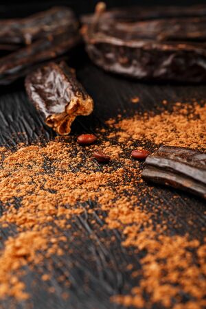 Carob carob fruit with powder on black background. Blast the Sweet powder from the pulp of the pods. Substitute cocoa and sugar, chocolate patients with diabetes and overweight people.の写真素材