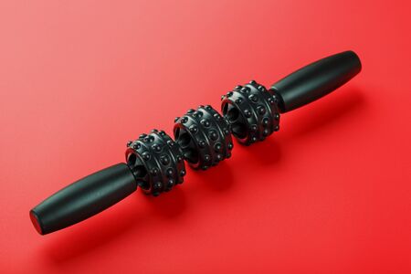 Black lumpy foam body massage roller on red background.の写真素材